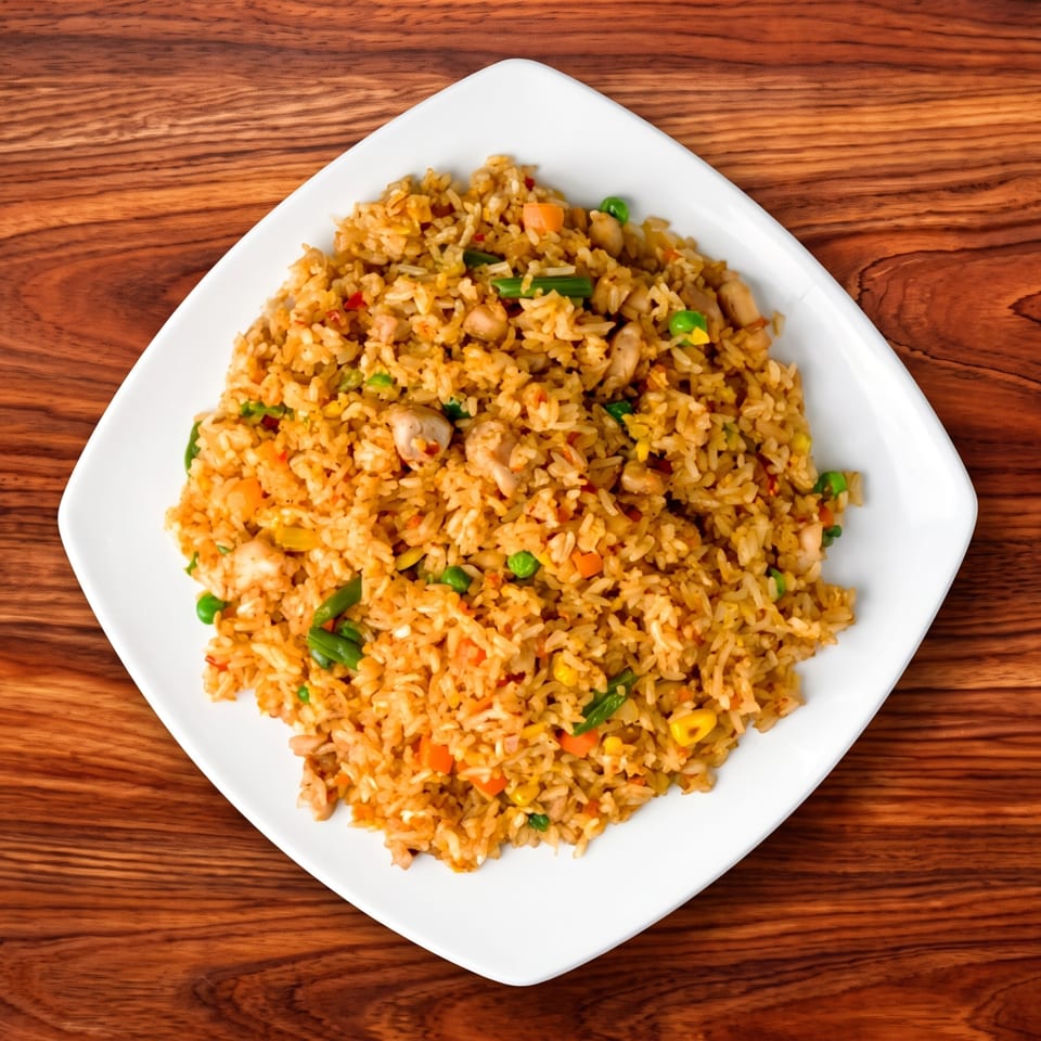 Chicken fried rice with peas, carrots, and corn on a white plate atop a wooden table.